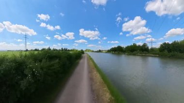 Bereketli yeşillik ve kabarık bulutlarla çevrelenmiş yumuşak bir nehir tarafından çevrelenmiş sakin bir yol mavi gökyüzüne karşı Wunstorf Kolenfeld Mittellandkanal