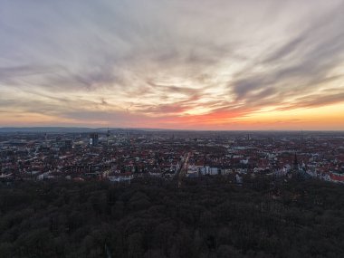 Gün batımının nefes kesici ve çarpıcı görüntüsü, canlı renkleri ve yumuşak bulutları ile şehrin ufkunu aydınlatan Hannover Aşağı Saksonya