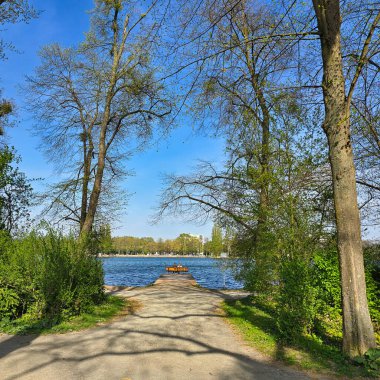 Sakin bir yol, bereketli ağaçlar ve masmavi bir gökyüzü altında canlı yeşilliklerle çerçevelenmiş pitoresk bir göle götürür.