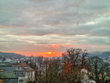 Büyüleyici, canlı bir günbatımı gökyüzünü aydınlatıyor. Ağaçlar ve bulutlarla süslenmiş büyüleyici bir kasaba. Bielefeld.