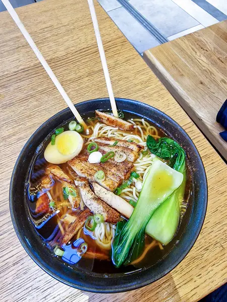 Yumuşak domuz etiyle kaplı sıcak bir kase ramen, kaynamış yumurta, sebze ve çubuklarla servis edilen erişte.