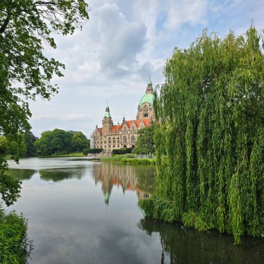 Bereketli yeşilliklerle çevrili sakin bir gölün yanında tarihi bir binanın bulunduğu sakin bir manzara. Maschpark Hannover
