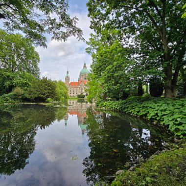 Nefes kesici bir manzara, sakin sularda yansıyan görkemli bir kaleyi gösteriyor. Canlı yeşil Maschpark Hannover ile çevrili.