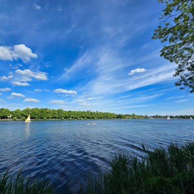 Huzurlu bir göl manzarası, canlı bulutlar ve yemyeşil, doğa aşıkları için ideal bir yer, Maschsee Hannover 'dan barışçıl bir kaçış arıyor.