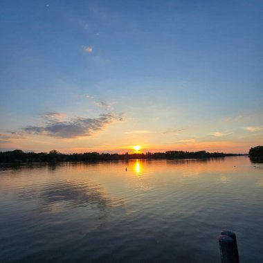 Sakin bir günbatımı, sakin sulara güzel bir şekilde yansıyor, doğanın muhteşem renklerini her yerde sergiliyor.