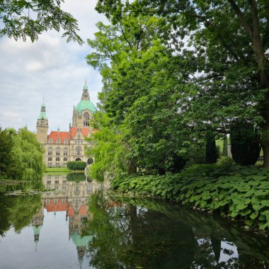 Bereketli yapraklar ve Maschsee Hannover 'ın canlı ağaçlarıyla çevrili sakin bir gölde yansıtılan antik bir kalenin çarpıcı görüntüsü.