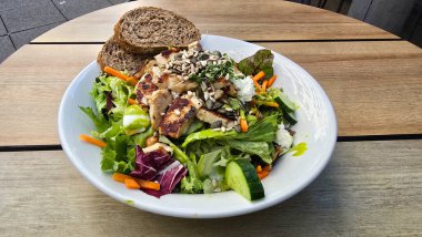 Bol bol kızarmış tavuk, çıtır çıtır tohumlar ve sağlıklı tahıl ekmeğiyle kaplanmış canlı yeşil bir salata.