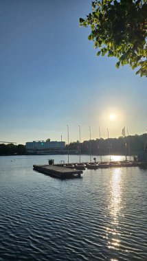 Huzurlu göl kenarında büyüleyici bir günbatımına tanık olun. Zarif yelkenliler ve parıldayan yansımalar Hannover Maschsee.