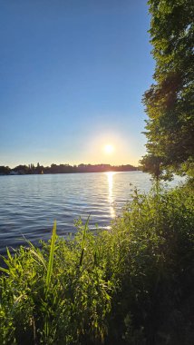 Gün batımında sakin ve huzurlu bir göl manzarası, baş döndürücü altın güneş yansımasını sergiliyor sakin sularda, Hannover Maschsee