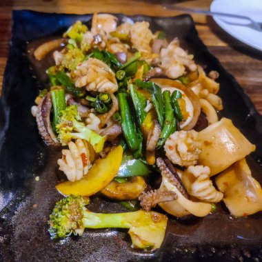 Brokoli ve diğer sebzelerle birlikte bir tabak kızarmış kalamar.