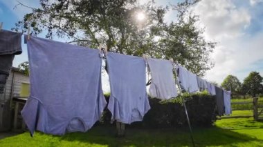 Güneşli bir günde açık hava ev işi sahnesi. Yeni yıkanmış giysiler, mavi gökyüzünün zemininde asılı duruyor. Bu görüntü temizliğin ve tazeliğin özünü yakalar..