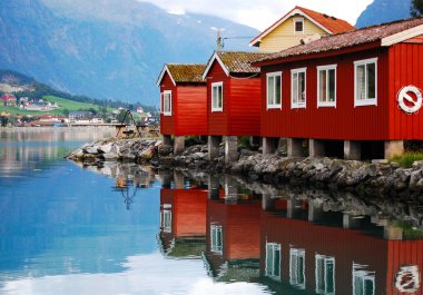 Norveç 'te fiyort kıyısındaki geleneksel ahşap kulübeler. Arka plandaki dağlarda ve küçük bir köydeki evlerde. Norveç manzarası