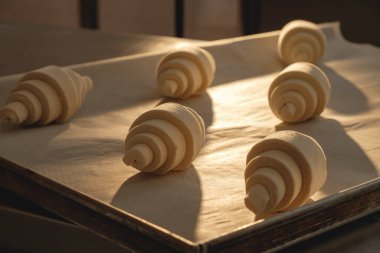 Sabahın ilk ışıklarındaki kruvasanlar sıcak bir fırının ahşap yüzeyinde pişmeyi bekliyor.