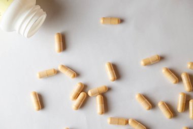 Dağıtılmış kapsüller yumuşak ışıkta pürüzsüz yüzeydeki bir şişeden dökülür.