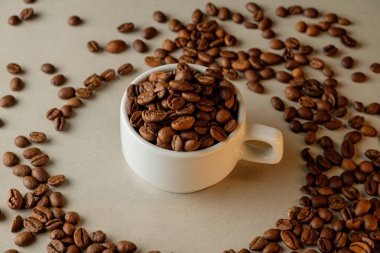 Kahve çekirdekleri dağınık fasulyelerle çevrili bir fincanda üst üste dizilmiş.