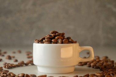 Kahve fincanı yumuşak ışıkta parlak bir yüzeyde kavrulmuş fasulyelerle dolup taşıyor.