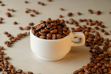 Kahve çekirdekleri, dağınık fasulyeli klasik beyaz bir fincanda üst üste yığılmış.