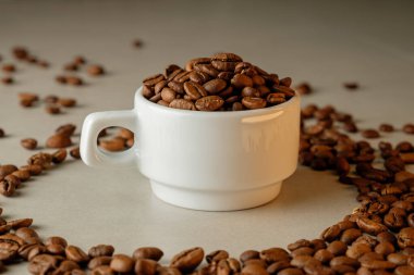 Kahve çekirdekleri, tezgahtaki dağınık fasulyelerin ortasındaki beyaz bardağı doldurur.