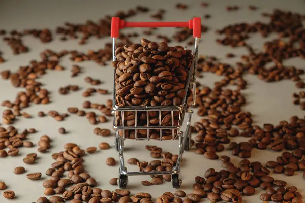 Hafif bir yüzey boyunca minyatür bir alışveriş arabasından kahve çekirdekleri taşar.
