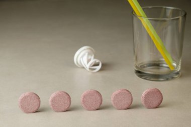 Renkli tabletler bir bardak ve bir kamışın yanında güzelce dizilmiş.