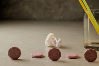 Renkli tabletler bir cam ve pipetin yanına dizilmiş.