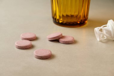 Kehribar rengi bir yüzeyde kehribar bir camın yanında pembe renkli haplar.