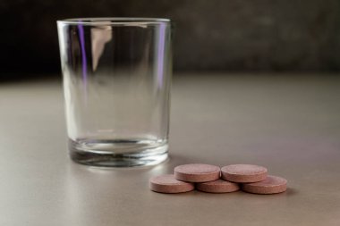 Temiz bir bardak, pürüzsüz gri bir yüzeyde pembe tabletlerin yanında boş duruyor.