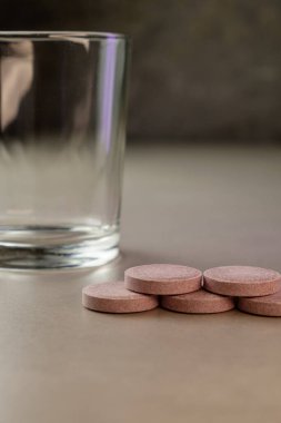 Pürüzsüz yuvarlak tabletler, açık bir bardağın yanına davet edilerek yerleştirilmiş.