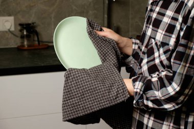 Elinde yeni temizlenmiş bir tabak tutan kişi mutfak havlusuna sarılmış.