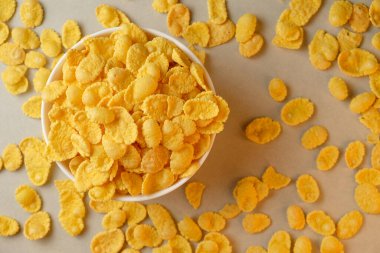 Parlak sarı mısır gevrekleri, çıtır çıtır bir kâseyle etrafa saçılmış.