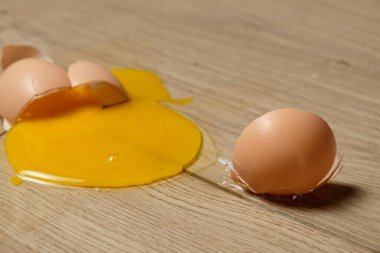 Çatlak bir yumurta, ahşap mutfak tezgahının üzerinde yatar. Parlak sarı sarısı, kabuğundaki yumurtanın tamamının yanına saçılır. Sahne yemek pişirirken mutfak kazalarının güzelliğini yakalar..