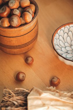 Kırsal ahşap bir kase zengin, kahverengi fındıkları taşırken narin desenli bir tabak yakınlarda duruyor. Ahşap masa sıcaklık katıyor, sıcak bir sonbahar atmosferini çağrıştırıyor ve doğanın cömertliğini içine davet ediyor..