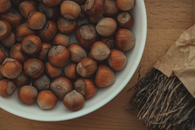 Zengin, kahverengi fındıkla dolu bir kase ahşap bir yüzeyde duruyor, iplikle bağlanmış taze otlarla çevrili, pişirme ve pişirme için mükemmel sıcak bir mutfak atmosferi sergiliyor..