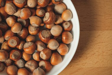 Parlak, kahverengi fındıkla dolu bir kase ahşap bir masada oturur. Her fındık pürüzsüz kabuğunu gösterir. İçindeki tadı gösterir. Yemek ya da atıştırmaya hazırdır..