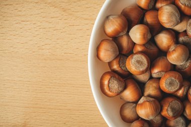 Taze toplanmış fındıkla dolu bir köy kasesi pürüzsüz bir ahşap masanın üzerinde duruyor. Zengin kahverengi fındıklar yumuşak bir şekilde parıldıyor. Sıcak ışıkta doğal güzelliklerine daha yakından bakıyorlar..