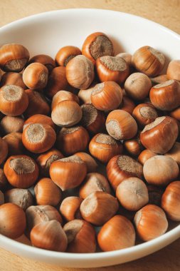 Taze, kavrulmuş fındıkla dolu bir kase ahşap bir yüzeyde duruyor. Zengin kahverengi renkleri ve pürüzsüz dokuları herkesi atıştırmalık ya da lezzetli tarifler almaya davet eder..