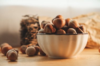 Taze toplanmış fındıkla dolu bir köy kasesi ahşap bir masanın üzerinde duruyor. Doğal ışık, fındıkların ve yakınlardaki kırsal dekorun toprak tonlarını vurgulayarak sıcak bir atmosfer yaratır..