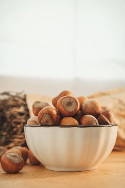 A ceramic bowl filled with fresh hazelnuts rests on a wooden table. The warm lighting enhances the natural colors, while a rustic backdrop adds charm to this simple display of natures bounty