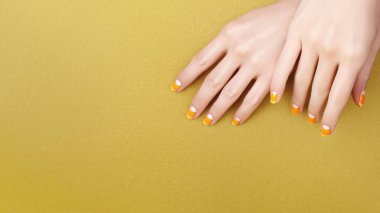 Beautiful Female Hands with bright Orange Manicure like Candy Corn on Yellow Background. Manicured Nails with Creative Gel Polish Design. Halloween Style