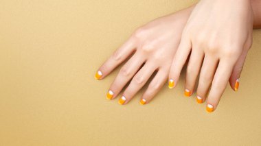 Beautiful Female Hands with bright Orange Manicure like Candy Corn on Yellow Background. Manicured Nails with Creative Gel Polish Design. Halloween Style