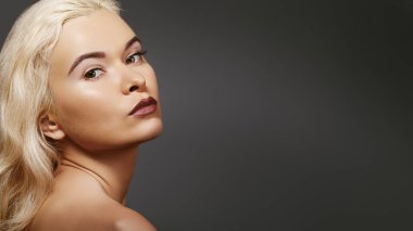 Geçmişe dönük seksi sarışın kadın portresi. Bej arka planda saf ciltli doğal güzellik. Moda makyajlı, saç stili, kadınsı bir kadın modeli.