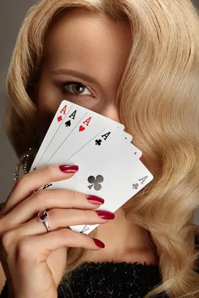 Kadınların elinde kağıt oynayan dört as. Poker dörtlü kombinasyonu olan bir oyuncu. Tırnaklarında kırmızı manikür olan zarif kadın elleri..