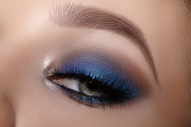 Parlak mavi dumanlı makyajlı kadın gözünün zarifliği. Kadın yüzünün makro görüntüsü. Güzellik, kozmetik ve makyaj