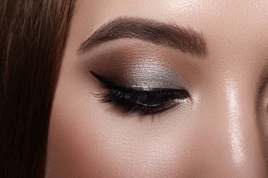 Klasik göz kalemi makyajlı güzel bir makro kadın gözü. Mükemmel kaşlar, kahverengi göz farı ve uzun kirpikleri. Makyaj malzemeleri ve makyaj malzemeleri. Moda gemisi bakışlarının yakın çekim makro çekimi.