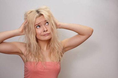 Dağınık saçlı ve suratını buruşturan suratlı mutsuz sarışın kadın. Çamaşır ve kuraklıktan dolayı kırılgan saç şekli zarar görmüş. Saç problemleri, güzellik sorunları, saç stili sorunları ve günlük rutin sorunlar. Stüdyo resmi