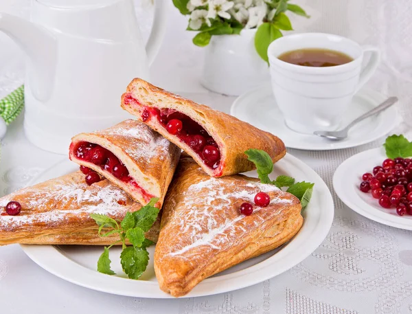 sweet pastries with red currant berries, with mint leaves, on a white dish, a cup of tea on a white background