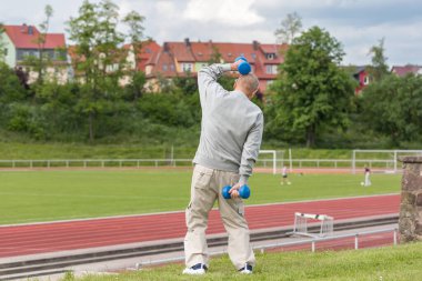 Yaşlı bir adam bir yaz akşamı stadyumun arka planında spor için içeri girer.