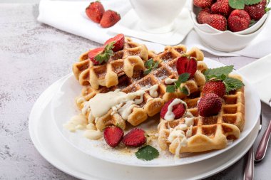 Viyana waffleları, beyaz bir tabakta açık güneşli bir arka planda çilekli.