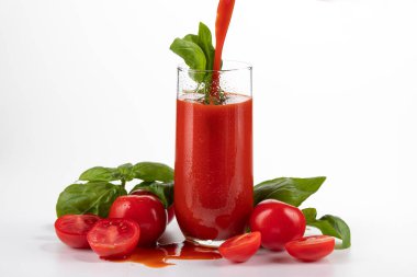 Bardakta domates suyu. Beyaz arka planda domatesler var.