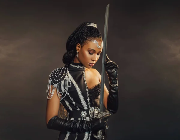 Portrait fantasy african american woman warrior holding sword weapon in hand. Dark queen girl in black military dress costume. Gothic lady elf fairy. Sexy beauty face fashion model pray. Studio photo.